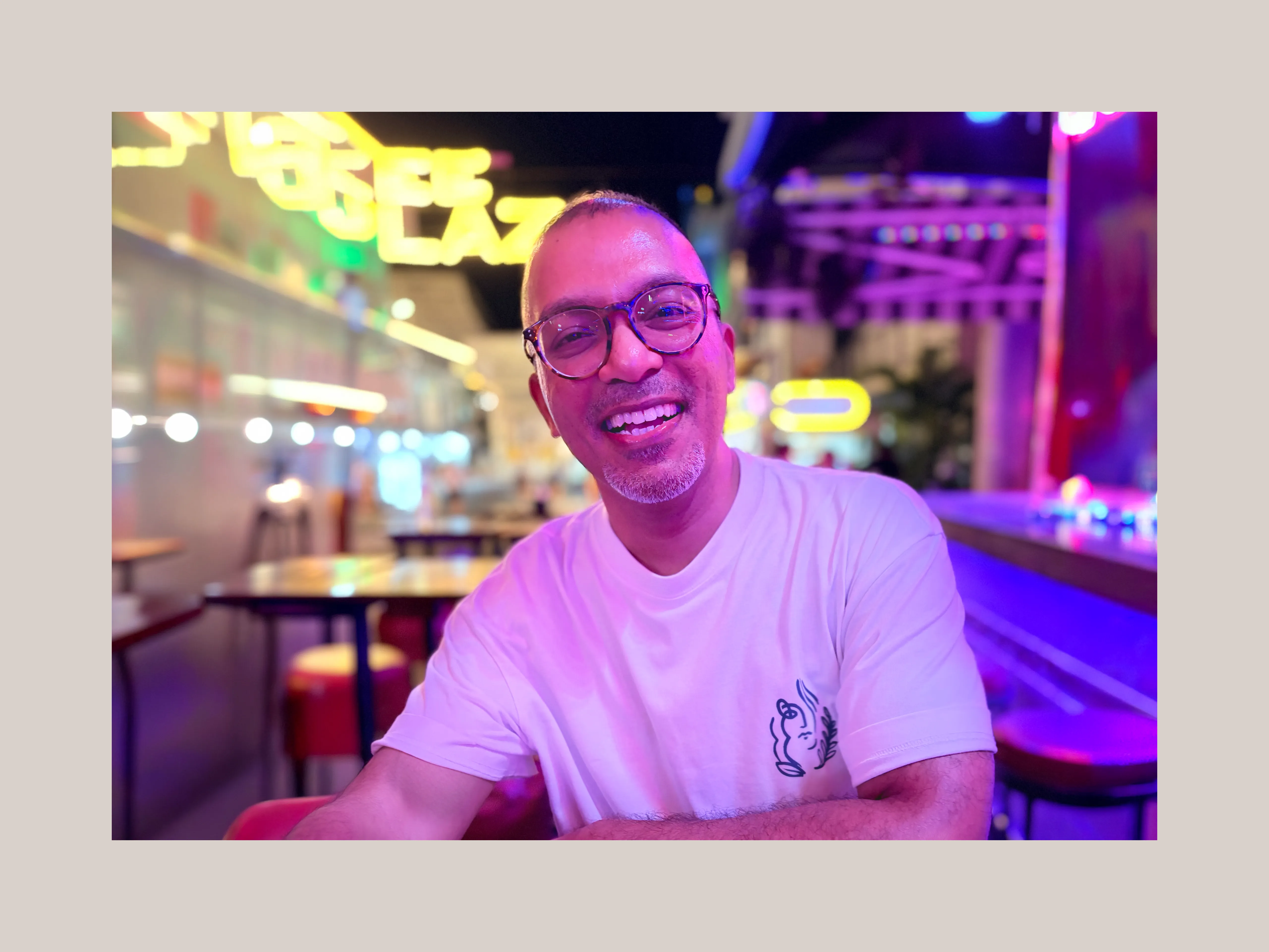 Geo George smiling, seated in a neon-lit arcade venue